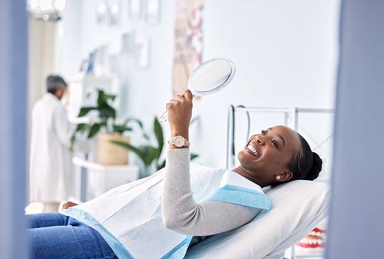 Reclined dental patient holding mirror, admiring her smile