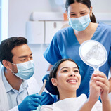 patient smiling at reflection next to dentist and dental assistant